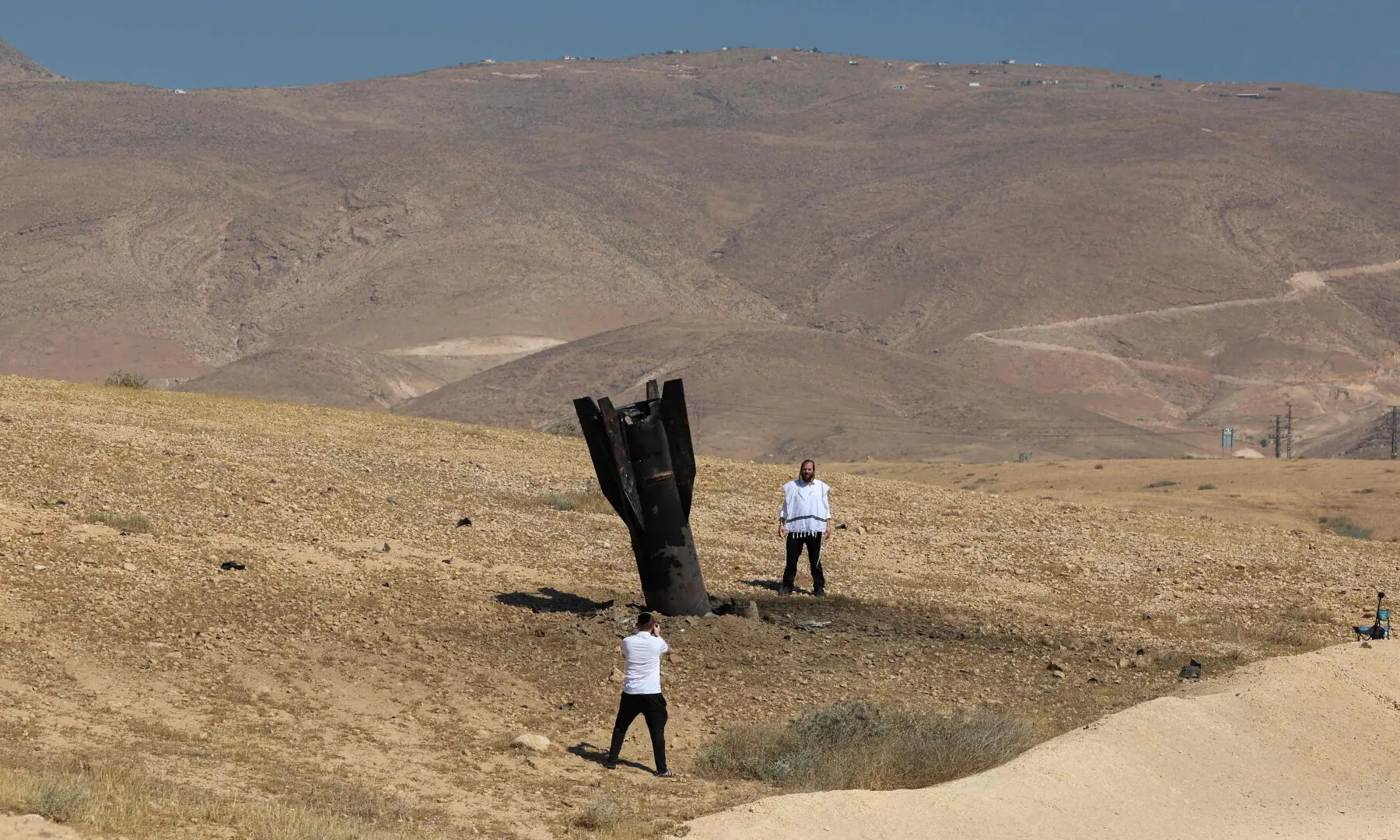  A man poses for a photo next to a fallen rocket half-buried in the ground on the outskirts of Jericho on June 8, 2026. &mdash; AFP 