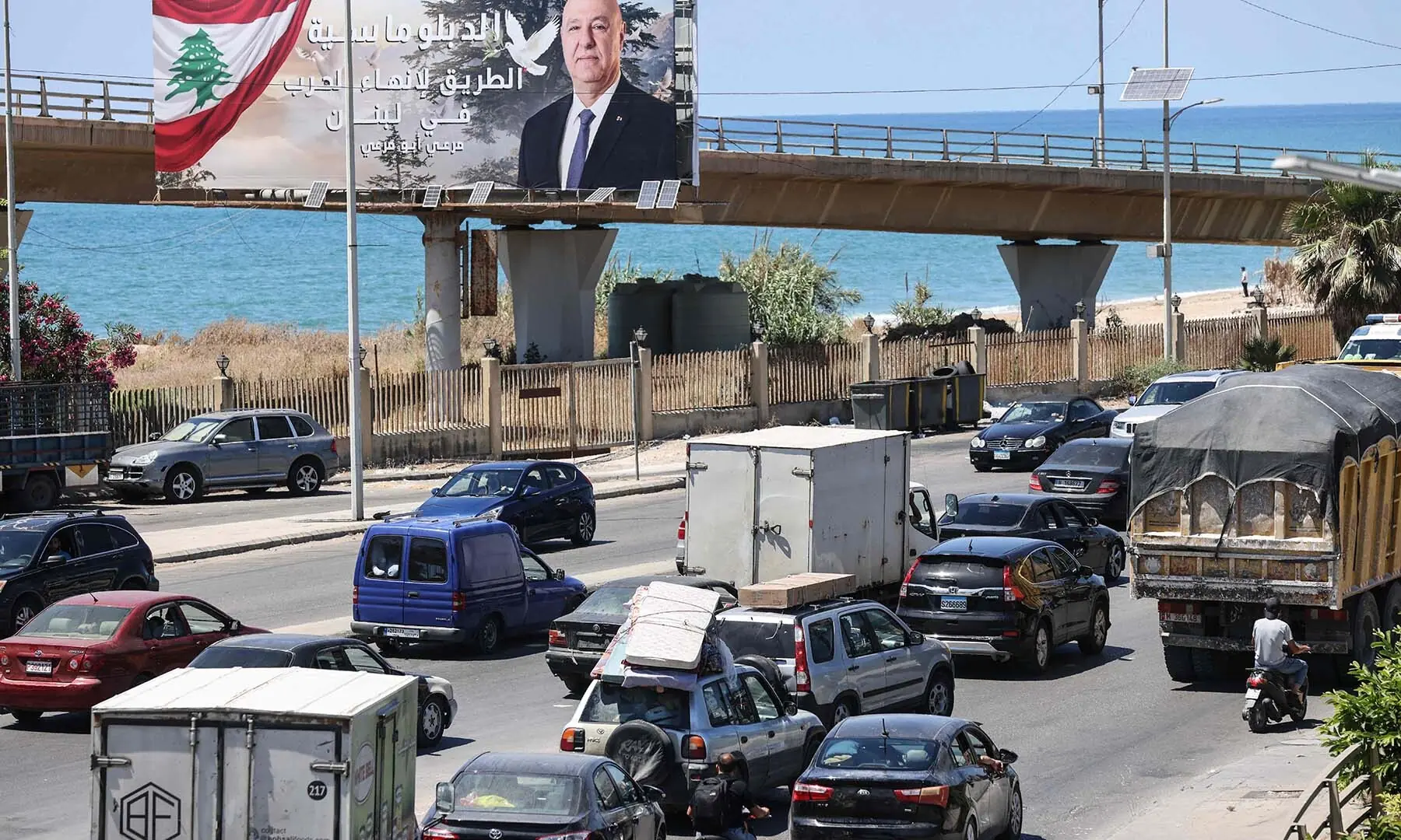 Vehicles drive past a billboard bearing a portrait of Lebanese President Joseph Aoun at the entrance to Sidon, Lebanon on June 19, 2026, as residents flee southern villages for the capital, Beirut, following Israeli airstrikes across the country&rsquo;s south. &mdash; AFP