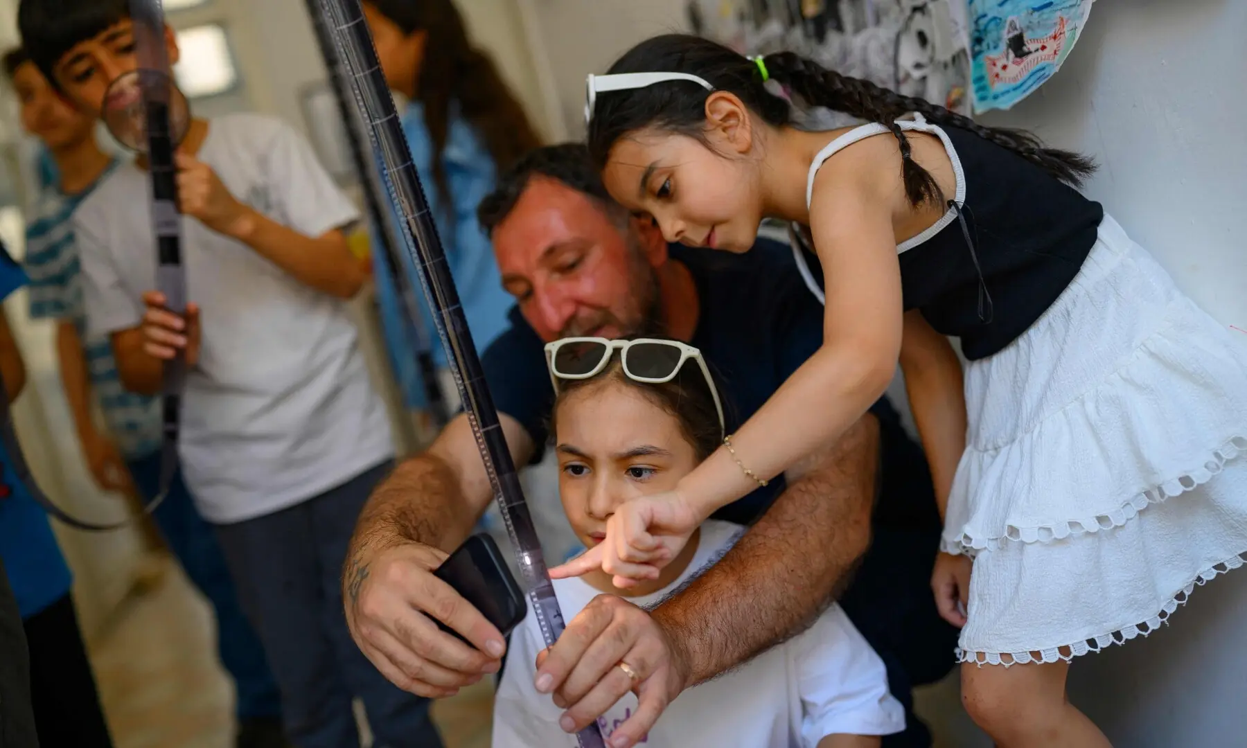 Zeynep (R) and Zuhre (C), 9-year-old, look at a camera film after developing it during a workshop held as part of Fotohane Darkroom project in Mardin, southeastern Turkiye, on June 13, 2026. — AFP