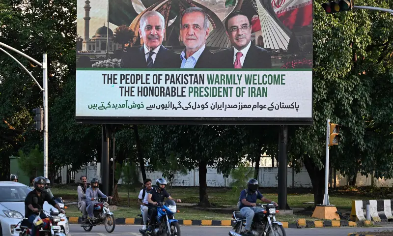 Commuters ride past an electronic board featuring Prime Minister Shehbaz Sharif (L), President Asif Ali Zardari (R) and Iran&rsquo;s President Masoud Pezeshkian (C), displayed along a street in Islamabad on June 22, 2026 on the eve of Pezeshkian&rsquo;s visit to Pakistan amid the US-Iran peace talks. &mdash; AFP