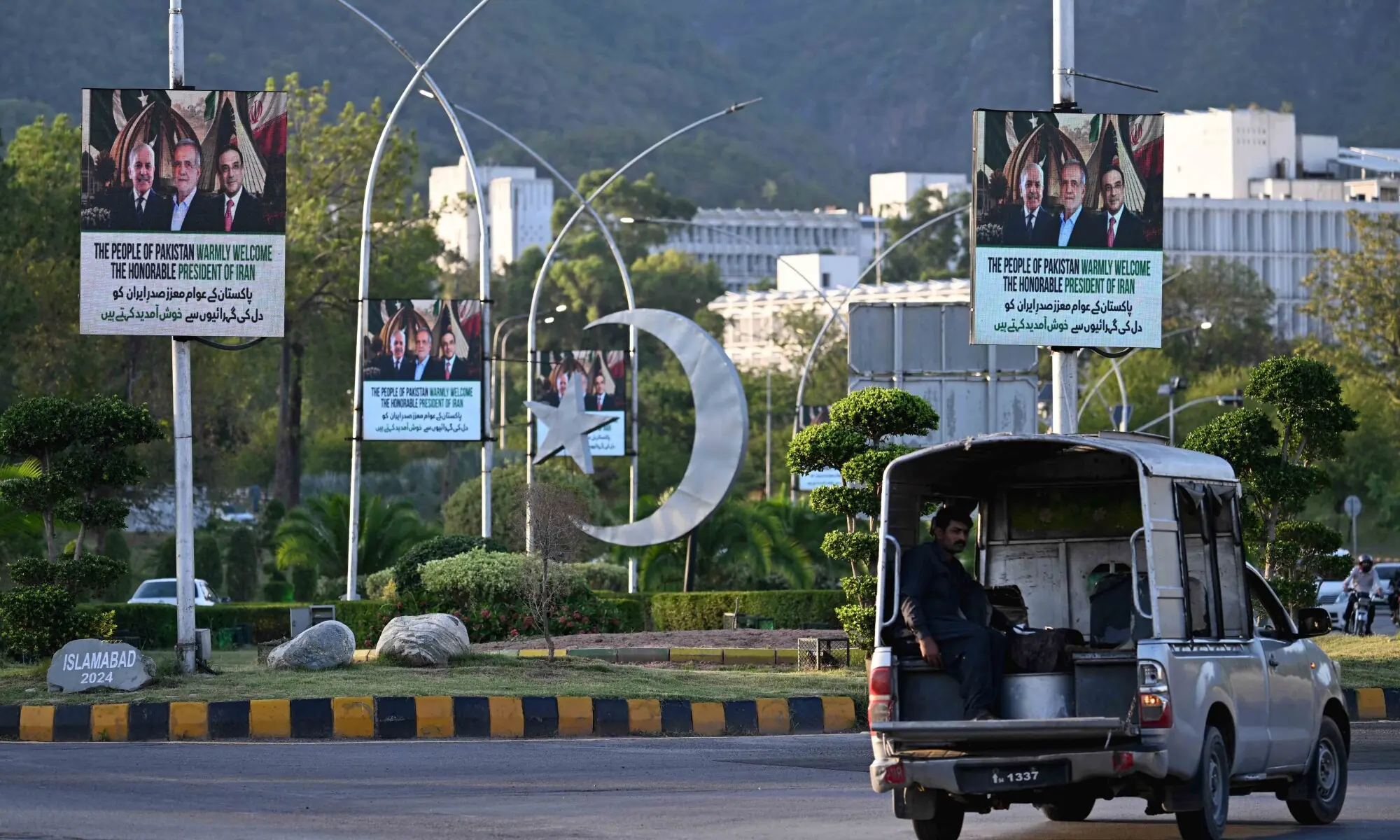 A commuter rides past electronic boards featuring Iran's President Masoud Pezeshkian (C), Prime Minister Shehbaz Sharif (L) and President Asif Ali Zardari, displayed along a street in Islamabad on June 22, 2026. &mdash; AFP