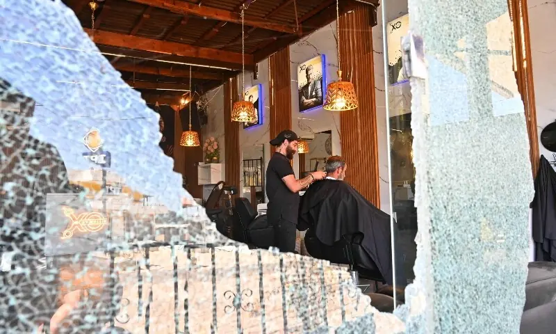A barber gives a haircut to a client at his saloon, damaged during Israeli military strikes, in the southern Lebanese village of Srifa on June 24, 2026. &mdash;AFP