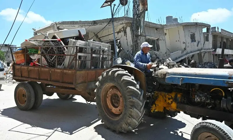 A man drives his tractor as it pulls a trailer laden with window frames and other salvaged goods past destroyed homes and businesses following Israeli military strikes, in the southern Lebanese village of Srifa on June 24, 2026. &mdash;AFP