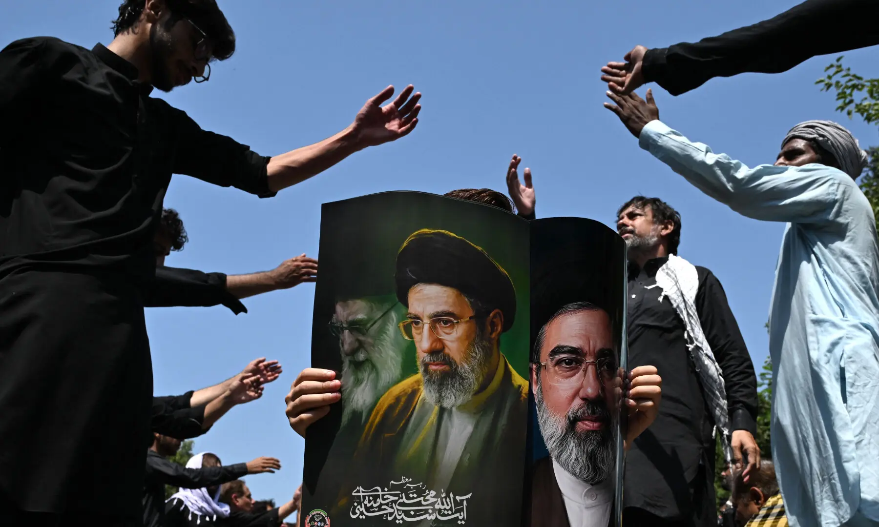 A person holds a poster with portraits of Iran&rsquo;s supreme leader Mojtaba Khamenei and late supreme leader Ayatollah Ali Khamenei (L) as mourners take part in a procession on the ninth day of Muharram in Islamabad on June 25, 2026. &mdash; AFP