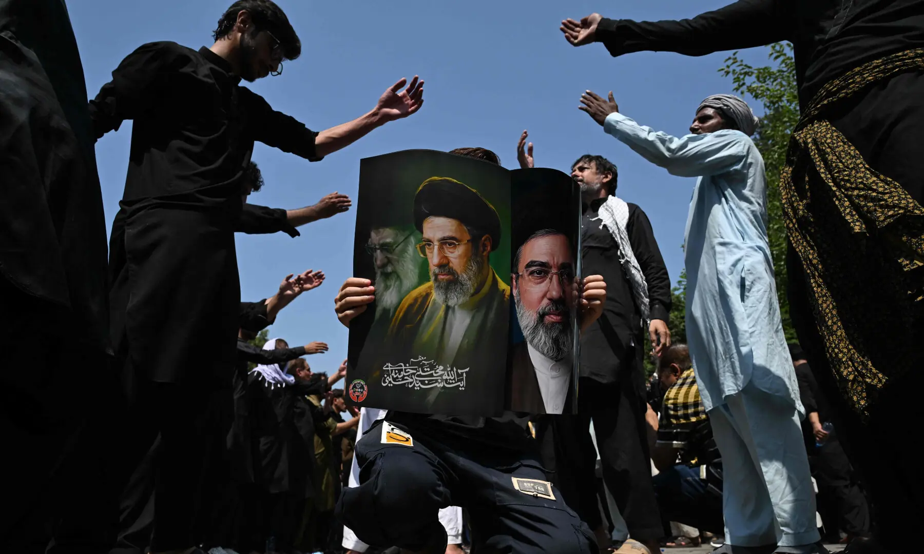 A person holds a poster with portraits of Iran&rsquo;s supreme leader Mojtaba Khamenei and late supreme leader Ayatollah Ali Khamenei (L) as mourners take part in a procession on the ninth day of Muharram in Islamabad on June 25, 2026. &mdash; AFP