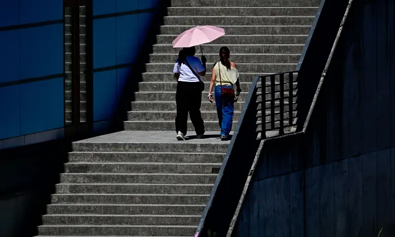 Two women shelter from sun with the help of an umbrella in the center of Berlin on June 26, 2026. &mdash; AFP