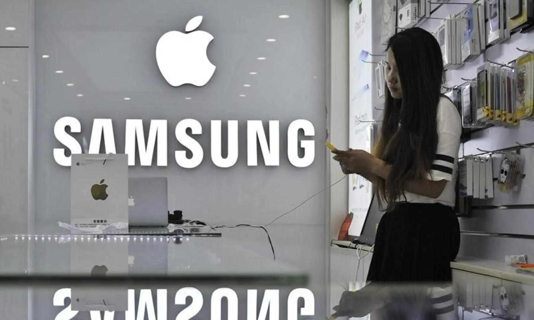 A sales assistant uses her mobile phone next to the company logos of Apple and Samsung at a store in Hefei, Anhui province, China on Sept 10, 2014. &mdash; Reuters/File