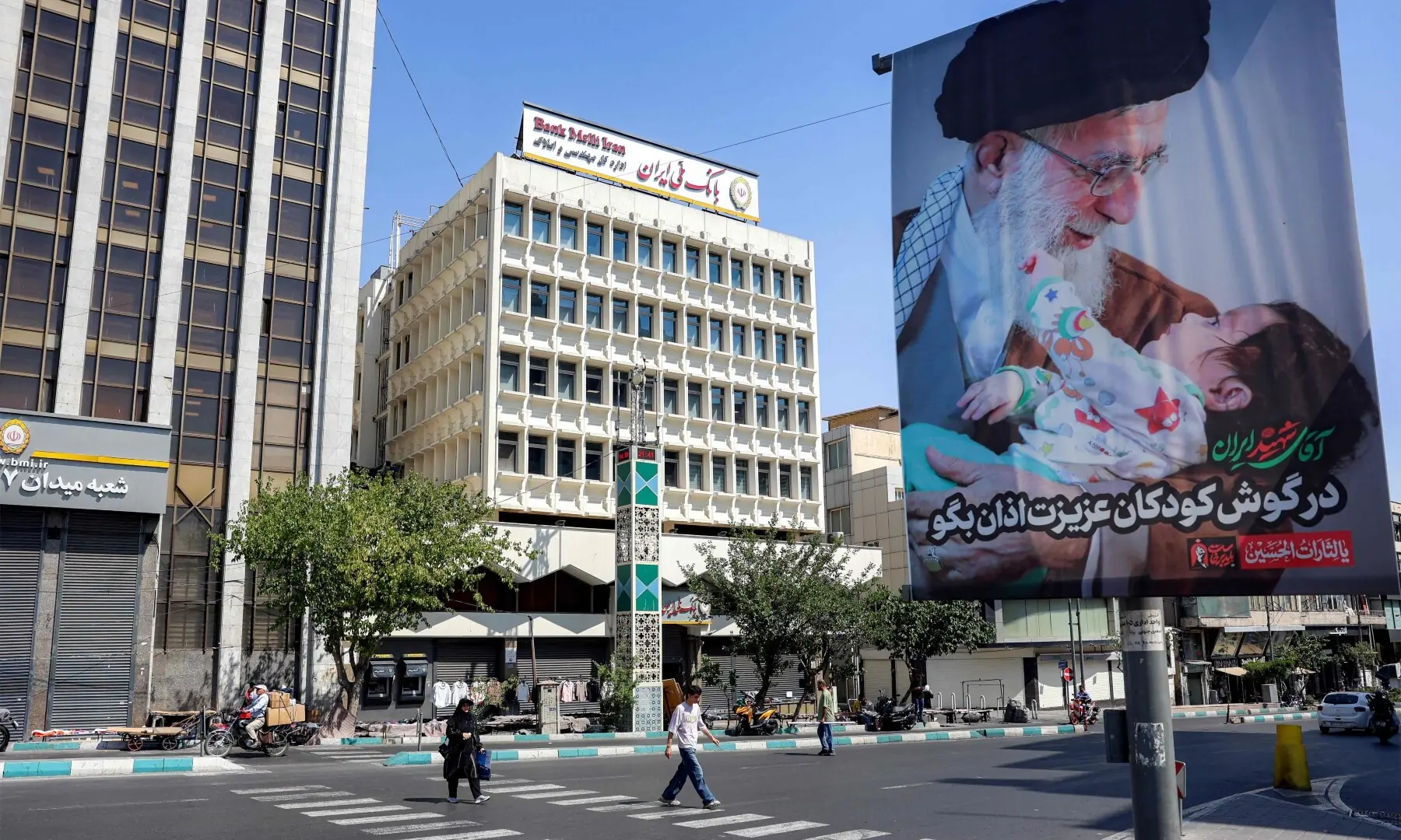 People cross a road past a mourning billboard depicting Iran&rsquo;s slain supreme leader Ali Khamenei, who was killed in a strike on the first day of the US-Israeli war against the Iran on February 28, in Tehran, Iran on June 30, 2026 ahead of his public funeral. &mdash; AFP