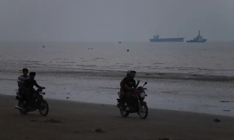 People ride motorbikes on the shore while vessels are in the Strait of Hormuz near the beach of Bandar Abbas, Iran, June 30, 2026. &mdash;Reuters