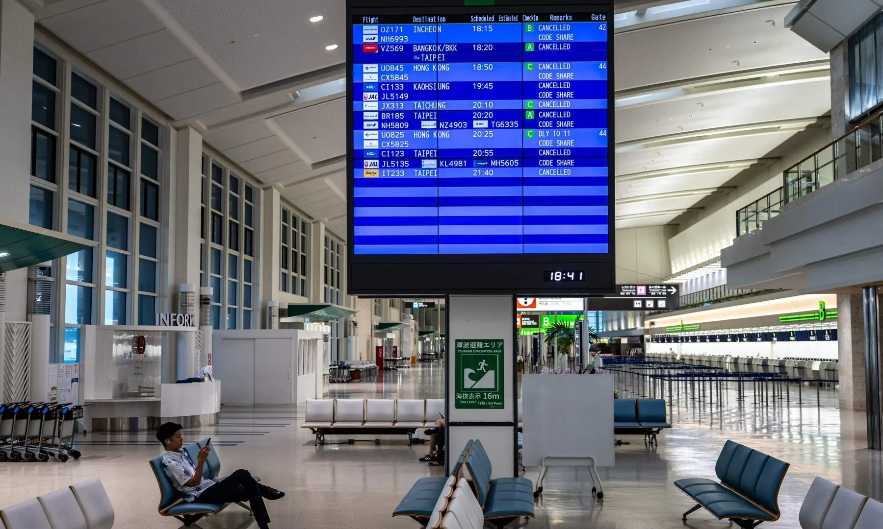A man sits next to a screen showing cancelled flights at the departure hall at Naha Airport in Naha, Okinawa prefecture, on July 10, 2026. —AFP