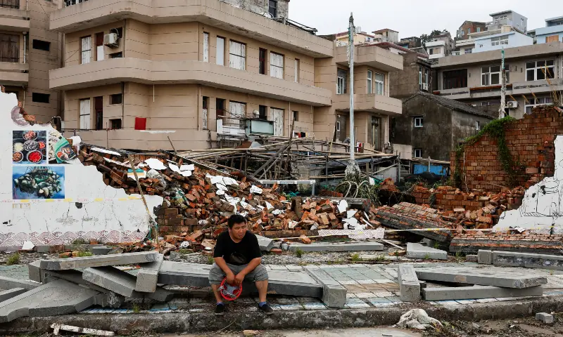 A person sits beside a collapsed wall in the aftermath of Typhoon Bavi in the coastal village of Dongsha, Taizhou, Zhejiang province, China, July 12, 2026. — Reuters