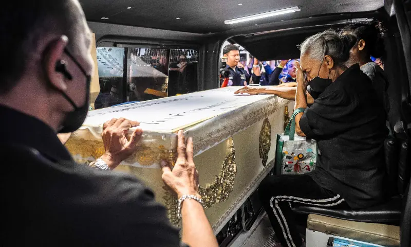 A relative (R) mourns next to a coffin bearing the remains of a victim killed in a bar fire, inside a hearse at the Police General Hospital in Bangkok on July 14, 2026. — AFP
