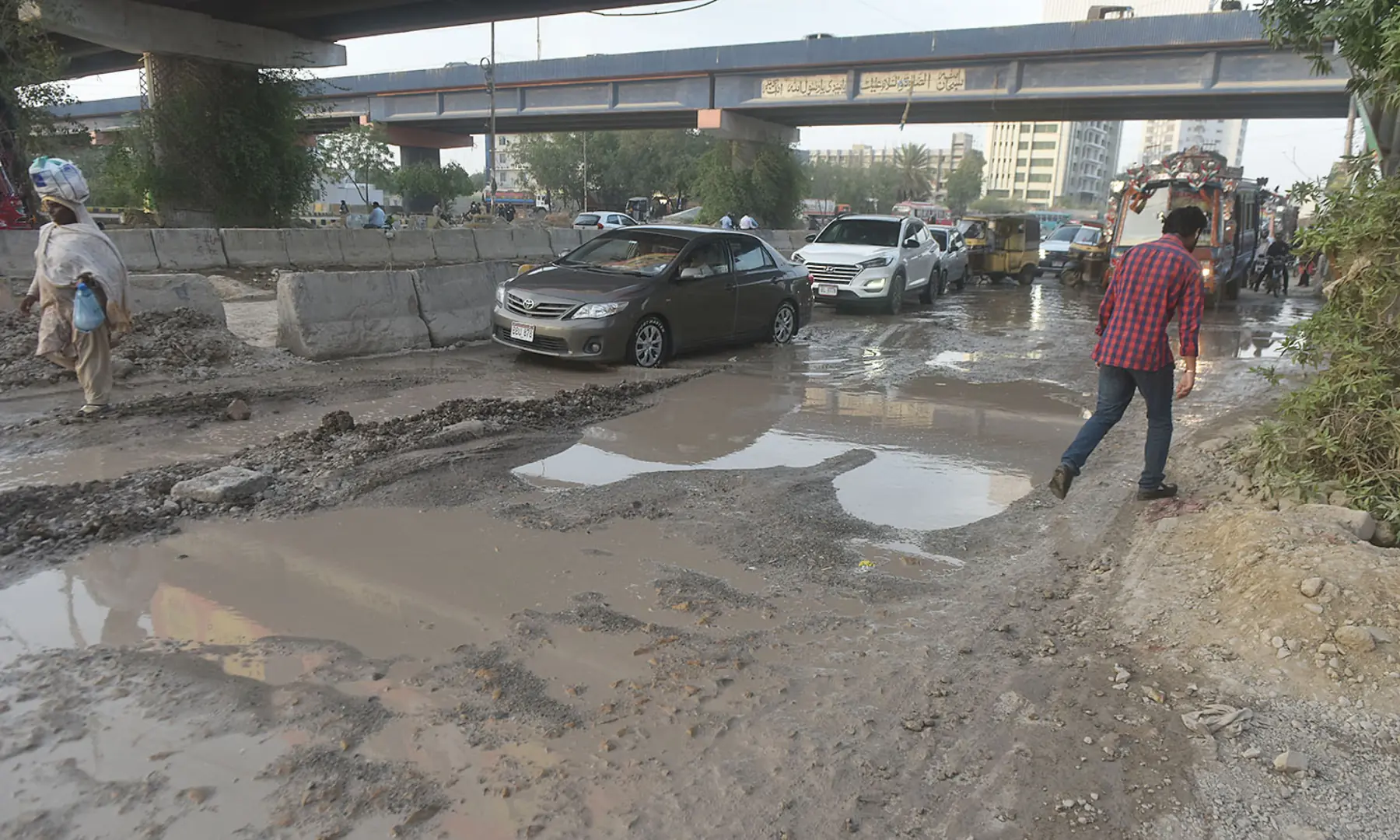 Cars drive single-file along a road that is mostly dug up in Karachi. &mdash; White Star