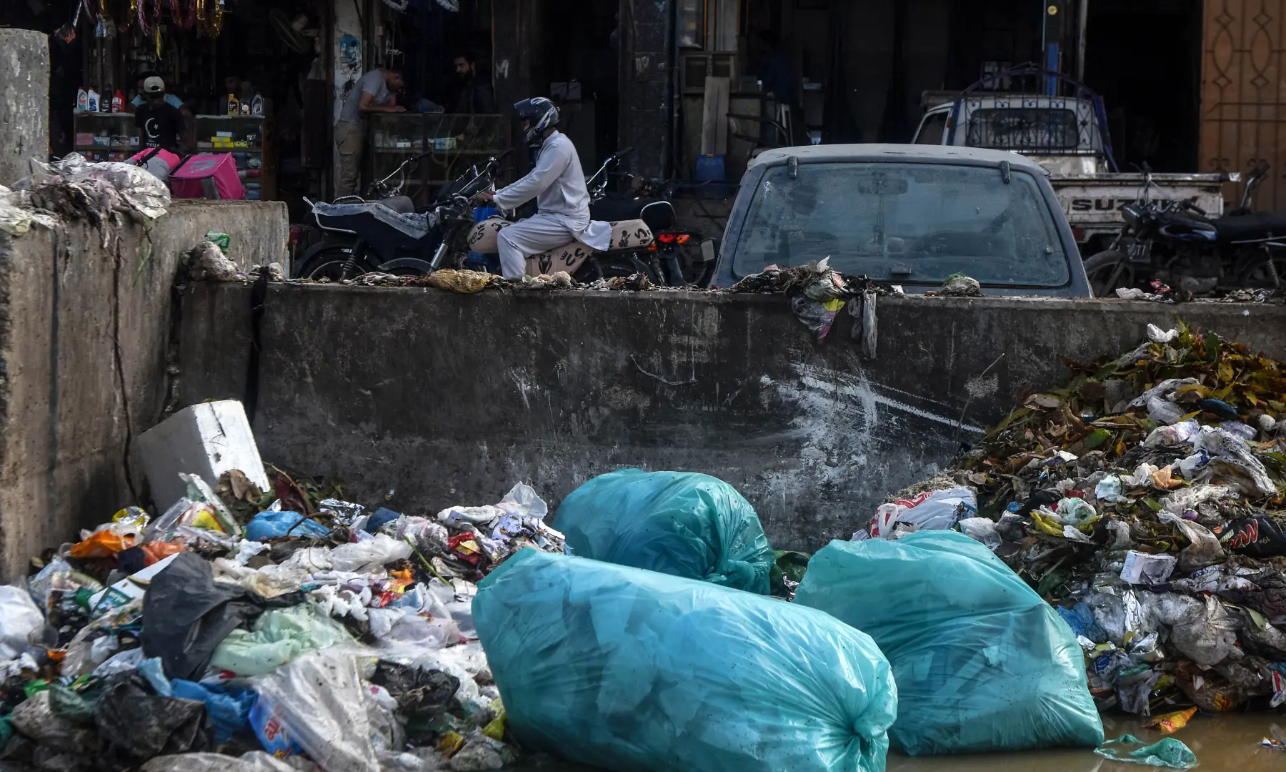 A motorcyclist rides past a pile of accumulated trash in a nullah in Karachi. &mdash; White Star