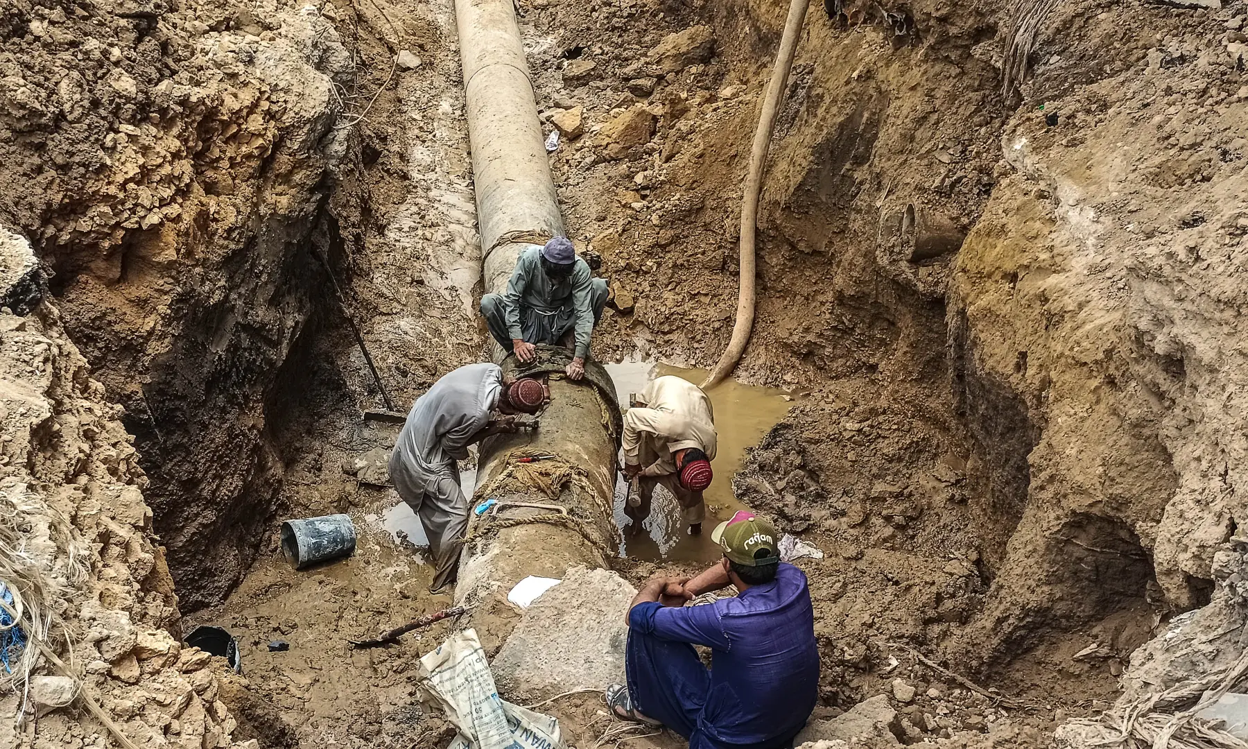 Workers carry out construction work on a pipeline under a dug-up road in Karachi. &mdash; White Star