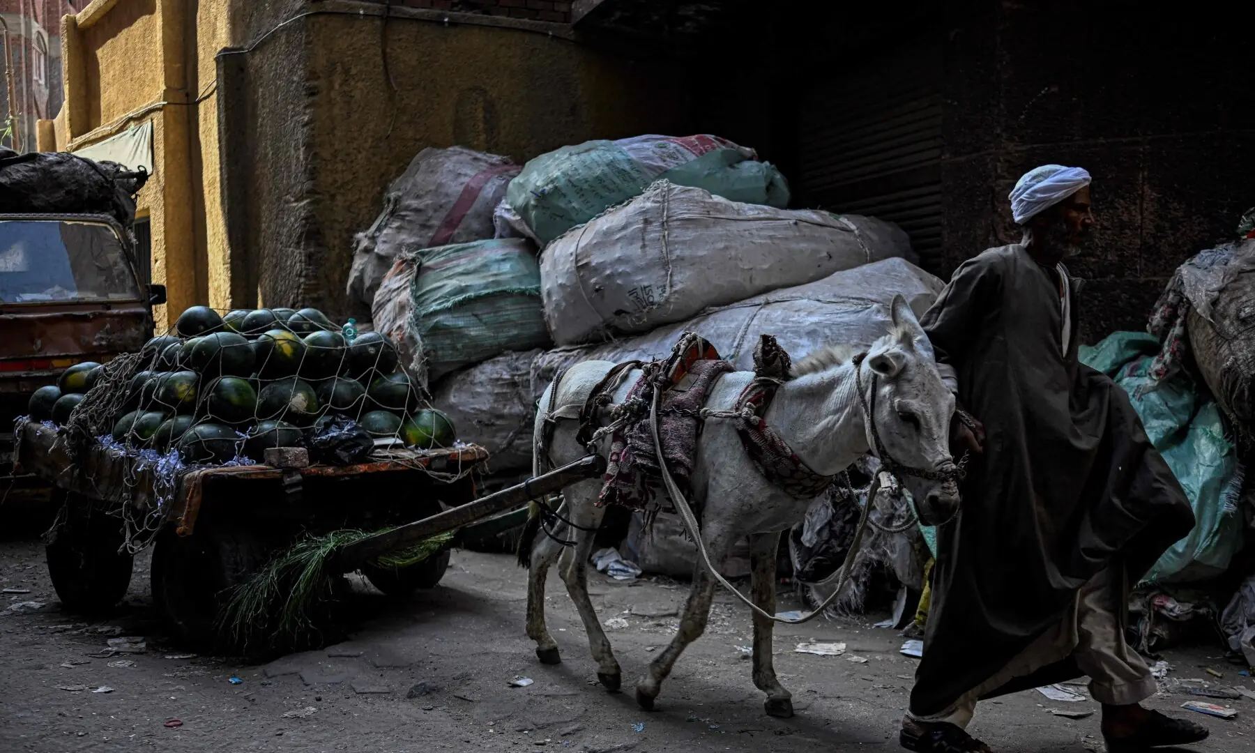 An Egyptian vendor leads his donkey cart loaded with watermelons past large bags filled with rubbish at the garbage city in the Manshiyet Nasser neighbourhood in Cairo on July 6, 2026. — AFP