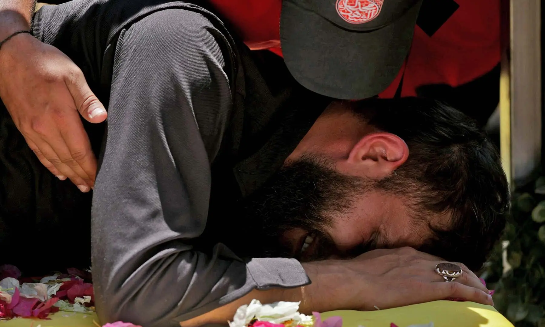 A man mourns as he lies on the casket of a Hezbollah fighter who was killed in clashes with the Israeli army during a mass funeral in the southern Lebanese village of Majdel Selm on July 18, 2026. &mdash; AFP