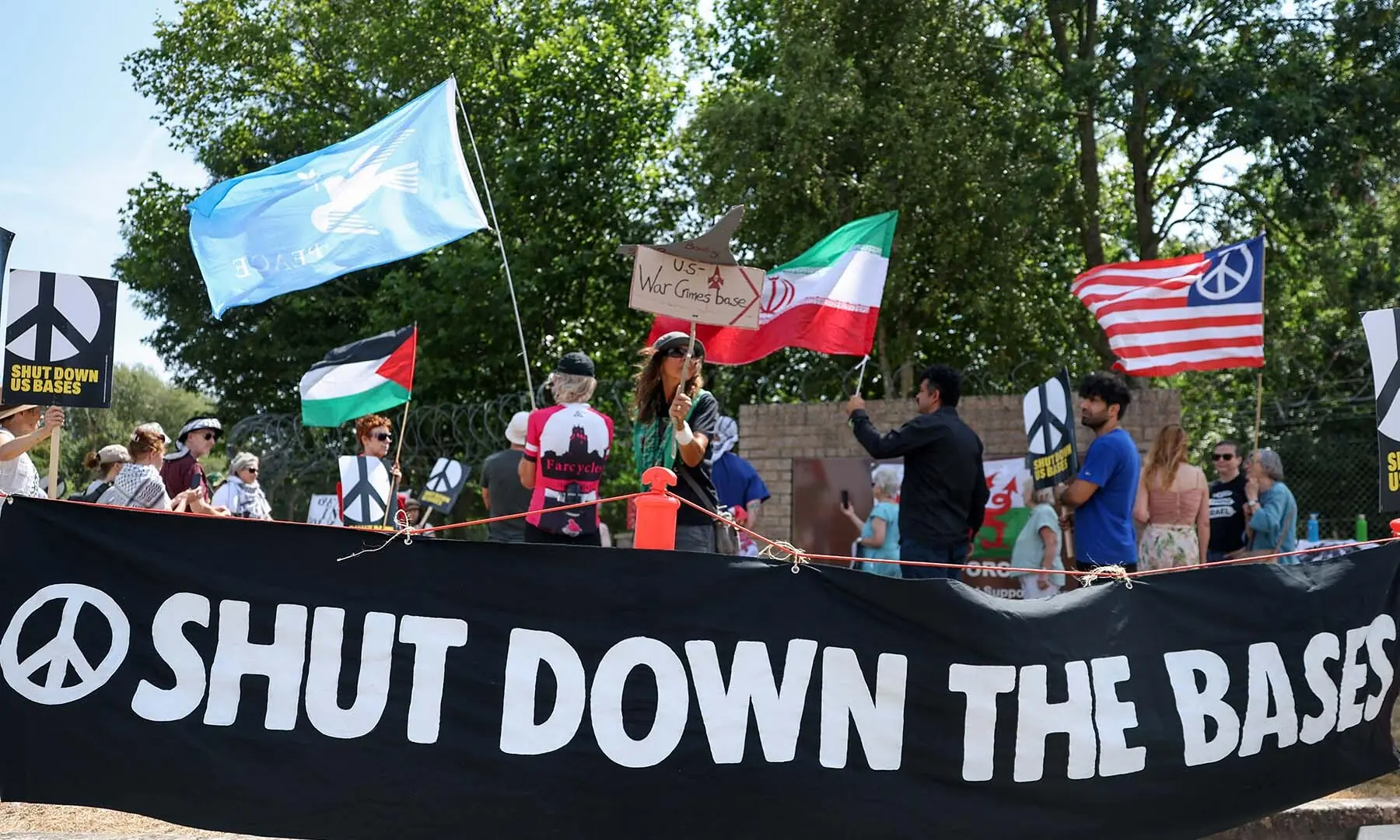 A banner with the slogan &lsquo;Shut down the bases&rsquo; is displayed near people with Iranian, Palestinian and other flags, during an anti-war demonstration outside the main gate of RAF Fairford airbase, which hosts US Air Force personnel in Fairford, Gloucestershire, the UK on July 25, 2026. &mdash; Reuters