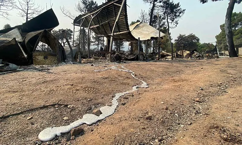 A trail of molten metal from a burnt-out vehicle is seen on the ground as charred remains of caravans and tents are seen following a wildfire at the Pantano de Burguillo campsite in El Barraco, 100 kilometres west of Madrid, Spain on July 27, 2026. — AFP