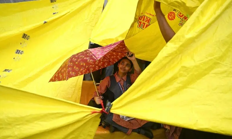 A school girl takes shelter under an umbrella at Jantar Mantar in New Delhi on July 24, 2026 during the ongoing Cockroach Janta Party (CJP) protest to demand the resignation of India's Education Minister Dharmendra Pradhan over alleged NEET exam irregularities. &mdash;AFP/File