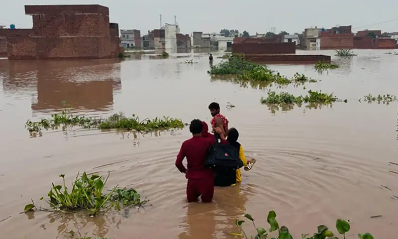 LAHORE: A family wades through floodwaters to pick up some items from their home in Rahim Colony, as they prepare to shift to a safe place after the Bhed Nullah overflowed, inundating the Ferozwala locality.&mdash;Khalid Hasnain