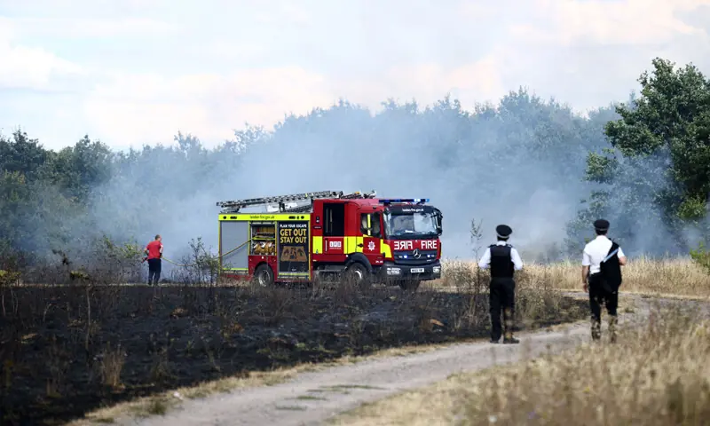 Police officials watch as a firefighter works at the site of a wildfire in Hornchurch, east of London.&mdash;AFP