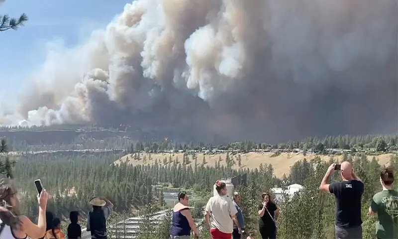 (LEFT) People watch as massive plumes of smoke rise from a wildfire in Spokane, US; while (right) firefighters battle a wildfire near the village Agia Paraskevi, Greece.&mdash;Reuters