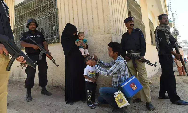 Policemen stand guard as a health worker administers polio drops to a child during a polio vaccination campaign after a day of an attack by gunmen in Karachi. ─ AFP/File Policemen stand guard as a health worker administers polio drops to a child during a polio vaccination campaign after a day of an attack by gunmen in Karachi. ─ AFP/File