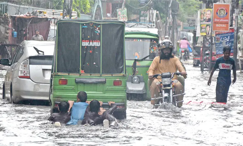 Children hold onto the rear of a rickshaw moving through rainwater on Naz Cinema Road after a heavy downpour in Rawalpindi on Monday. — Online Children hold onto the rear of a rickshaw moving through rainwater on Naz Cinema Road after a heavy downpour in Rawalpindi on Monday. — Online