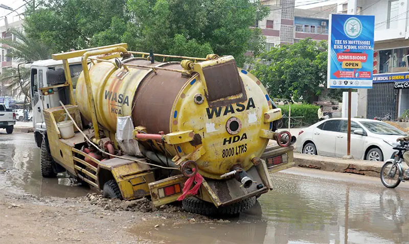 A DEWATERING vehicle of the Hyderabad Water and Sewerage Corporation gets stuck in a pothole along a flooded road in Latifabad Unit No. 8.—Dawn A DEWATERING vehicle of the Hyderabad Water and Sewerage Corporation gets stuck in a pothole along a flooded road in Latifabad Unit No. 8.—Dawn