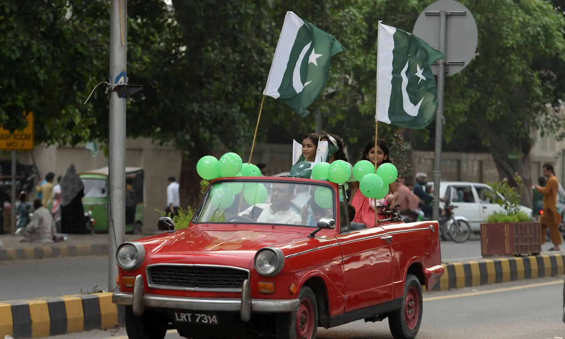 Green balloons and Pakistan flags are seen tied to a car driving along Mall Road in Lahore on Aug 14, 2026. &mdash; White Star