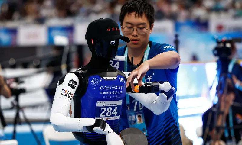 An engineer puts a ping pong ball in the hand of a humanoid by AgiBot during a ping pong contest at the 2026 World Humanoid Robot Games, at the National Speed Skating Oval, in Beijing, China on August 23, 2026. &mdash; Reuters