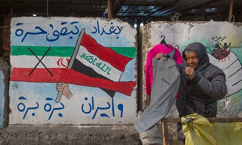 A street vendor displays clothes next to graffiti with Arabic that reads, "Baghdad is free and Iran out," in Tahrir Square, Baghdad, Iraq, on Wednesday. &mdash; AP/File
