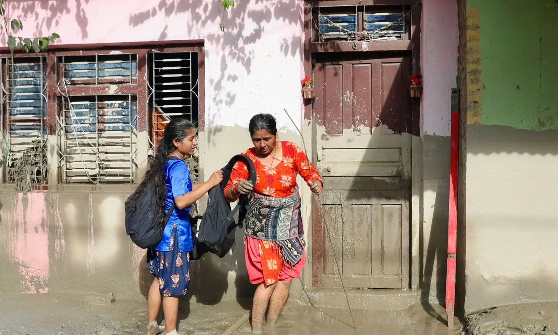  Women walk past a house bearing sludge marks that show the water level after flash floods near Devighat, Bidur Municipality in Nepal&rsquo;s Nuwakot district on Aug 27, 2026. &mdash; AFP 