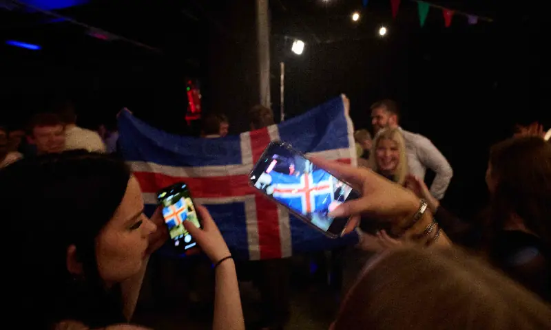 Women take pictures with their mobile phones as supporters wave an Icelandic flag during a referendum night event organised by Sfram Island, the &ldquo;No&rdquo; campaign against resuming Iceland's European Union accession negotiations, in Reykjavik, Iceland, on Aug 30, 2026. &mdash; AFP