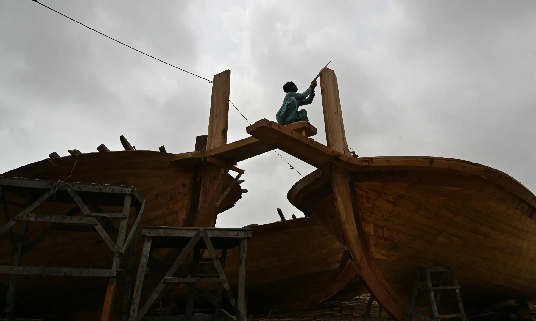 This photograph taken on July 8, 2026 shows a worker building a traditional wooden boat at a yard in Ibrahim Hyderi in Karachi. &mdash;AFP/File