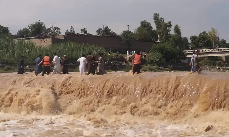 Rescue workers help stranded people cross rainwater overflowing a road after heavy rain in Bajaur on Tuesday. — Dawn Rescue workers help stranded people cross rainwater overflowing a road after heavy rain in Bajaur on Tuesday. — Dawn