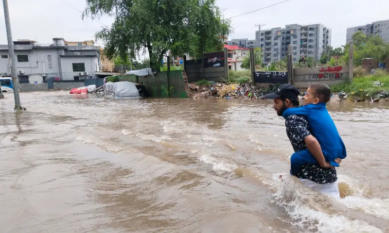 A man carries his child on his back as he wades through floodwater, after heavy rains lashed Rawalpindi on September 1. — White Star A man carries his child on his back as he wades through floodwater, after heavy rains lashed Rawalpindi on September 1. — White Star