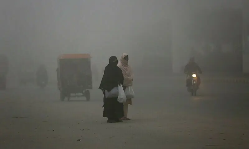 Women wait for transportation as heavy fog reduces visibility, in Lahore. &mdash; AFP