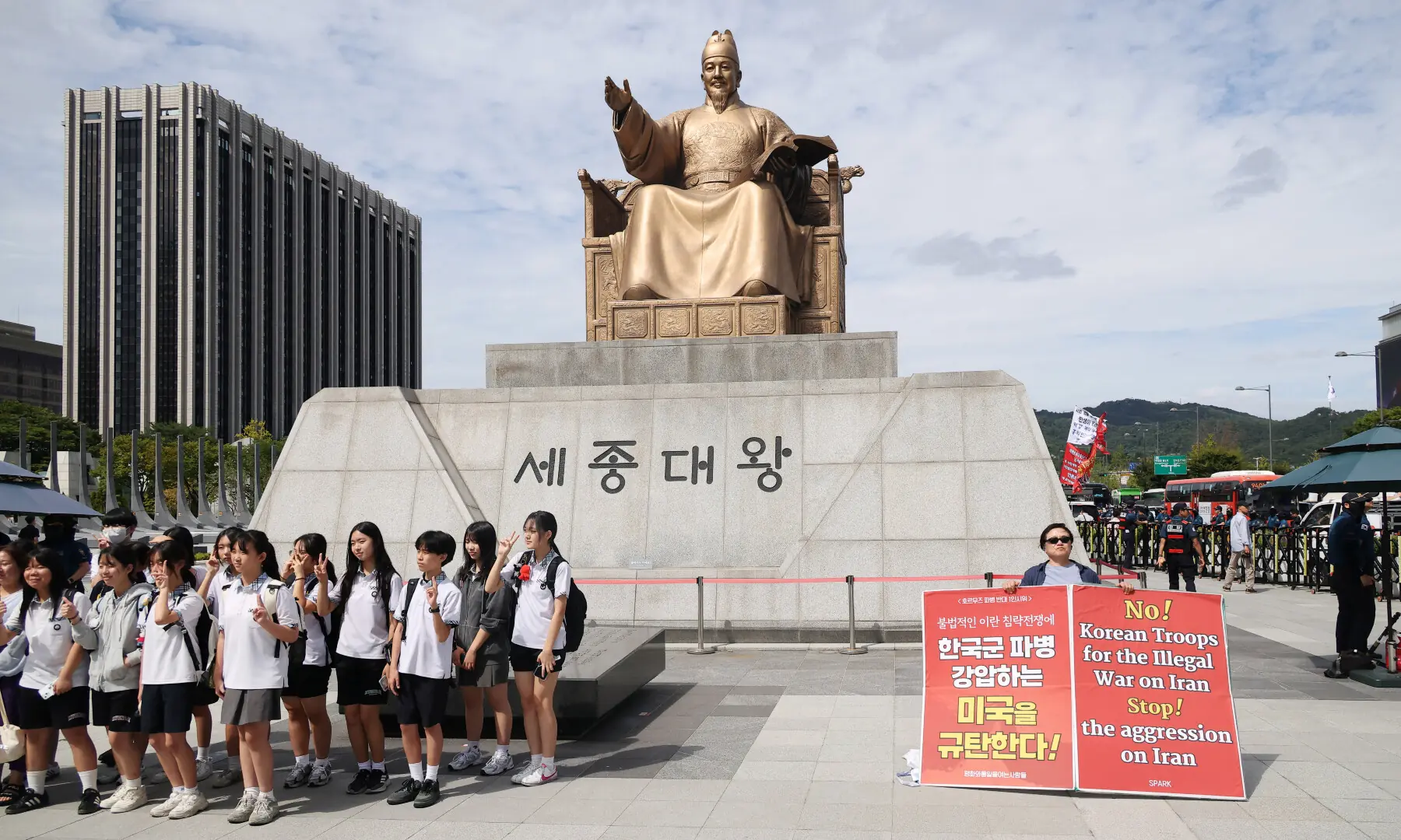 An activist holds a placard denouncing South Korea&rsquo;s possible military participation in the Strait of Hormuz, as a group of students pose for a souvenir photo in front of the Statue of King Sejong the Great, in Seoul, South Korea, on Sept 9, 2026. &mdash; Reuters