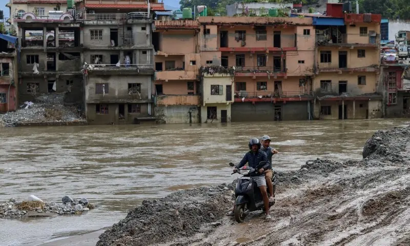 A motorcyclist rides through thick mud with flood-damaged houses in the background following deadly flash floods and a mudslide, in Devighat, Nuwakot district, Nepal, September 11. &mdash; Reuters
