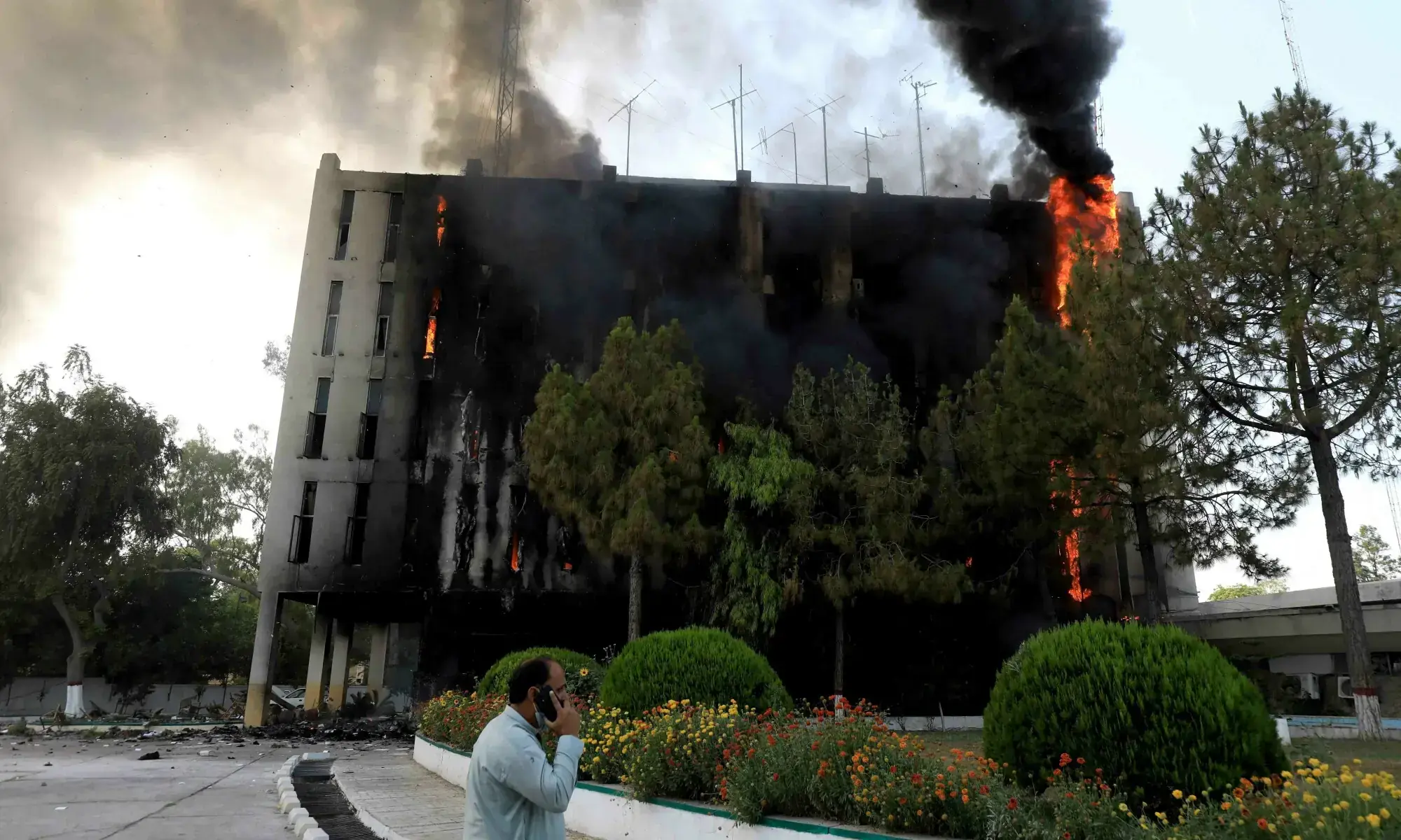 A man speaks on his mobile as fire and smoke billow from a Radio Pakistan building in Peshawar on May 10, 2023. &mdash; Reuters/File