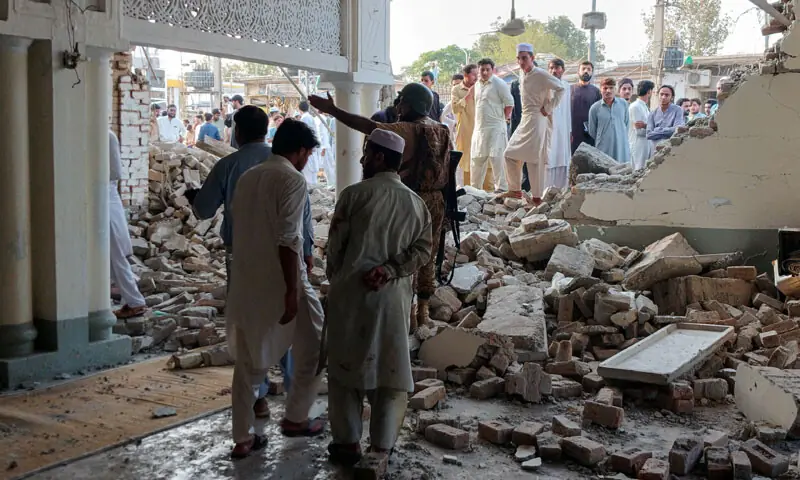 A SECURITY official tries to secure the crime scene as people gather to examine the damage to a mosque, following a gun-and-bomb attack on Kohat&rsquo;s Police Lines.&mdash;Reuters