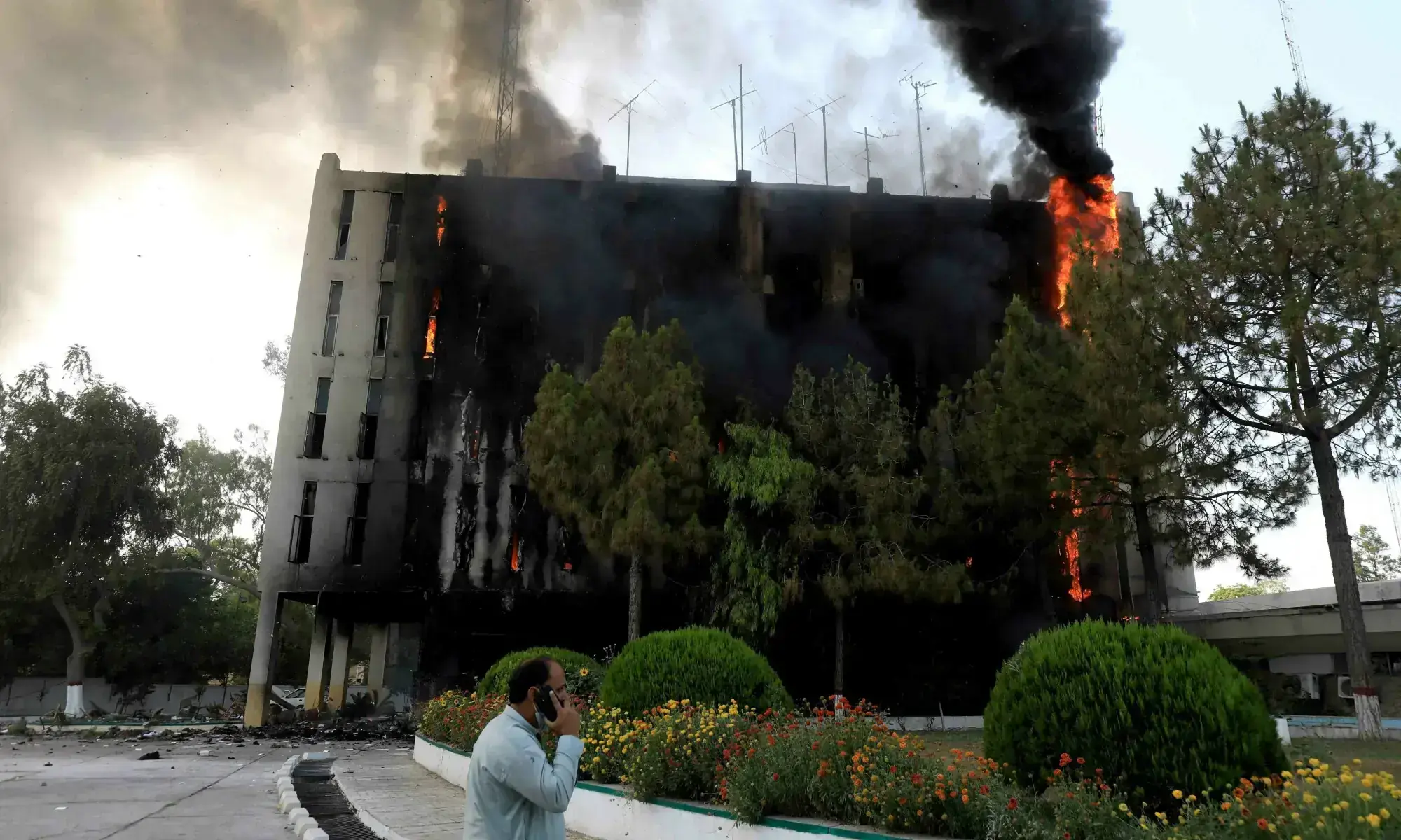 A man speaks on his mobile as fire and smoke billow from a Radio Pakistan building in Peshawar on May 10, 2023. &mdash; Reuters/File