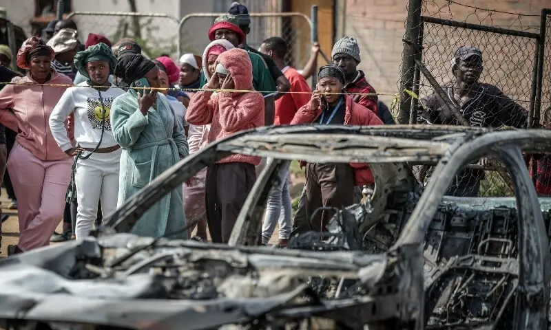 Residents stand behind police tape near the scene where gunmen armed with assault rifles stormed a bar in Johannesburg on September 27. &mdash; AFP