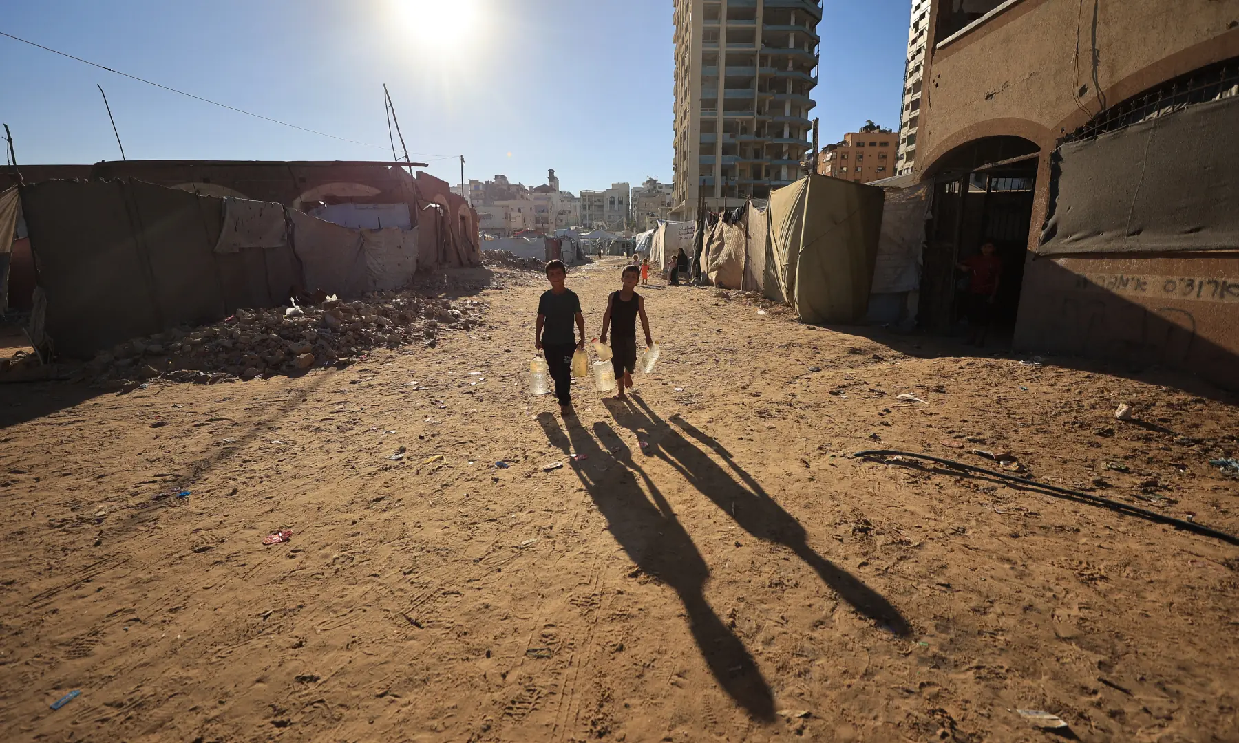 Children of displaced Palestinians, carry water containers to their temporary tents in Gaza City on Oct 7, 2026. &mdash; AFP