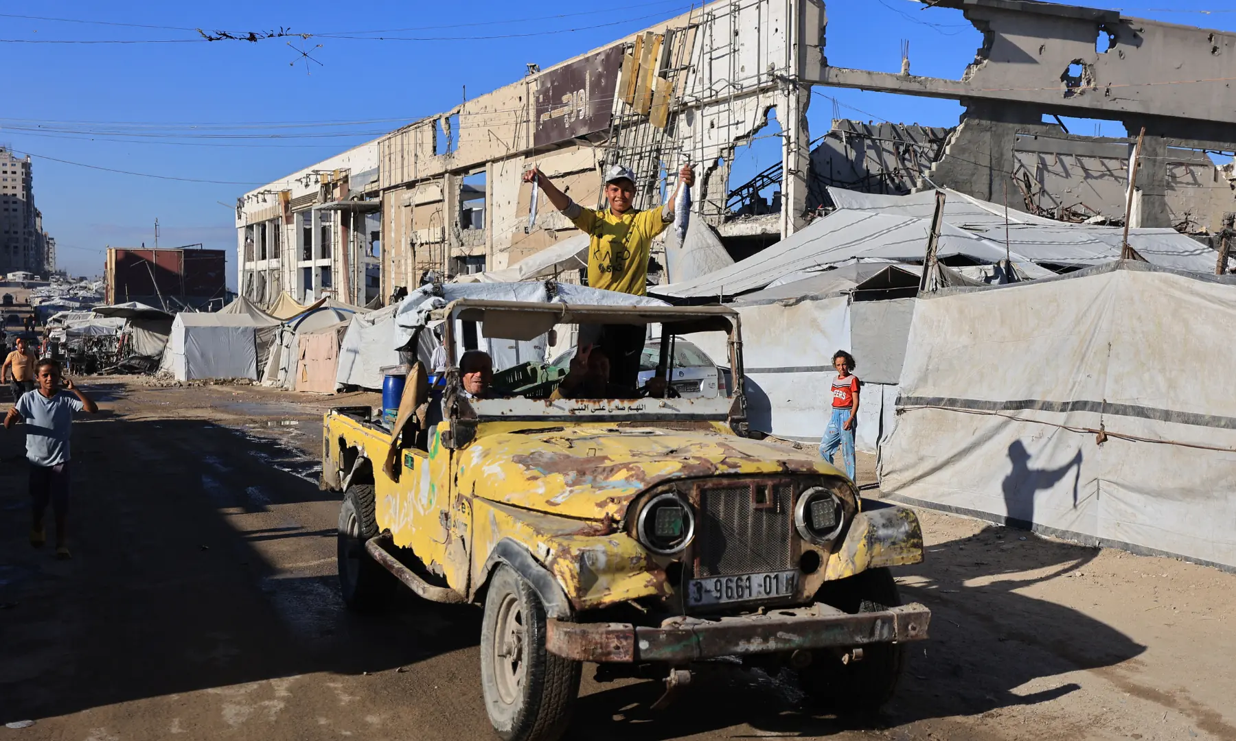 A boy displays fish while riding a jeep along the street lined with destroyed buildings and temporary tents of displaced Palestinians, in Gaza City on Oct 7, 2026. &mdash; AFP