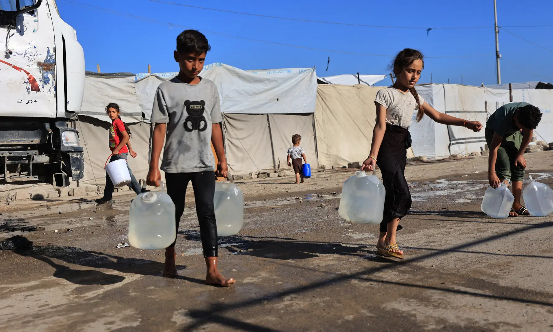 Children of displaced Palestinians carry water containers outside their temporary tents in Gaza City on Oct 7, 2026. &mdash; AFP