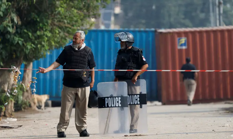 Police personnel stand guard near shipping containers blocking a road leading to the Red Zone in Peshawar on October 11, 2026. — Reuters