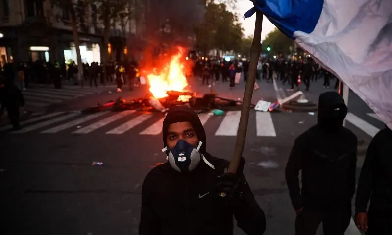 A protestor with a gas mask holds a French flag in front of a fire at the Boulevard des Capucines during a demonstration to protest against the “high cost of living”, in Paris, France on October 17, 2026. — AFP